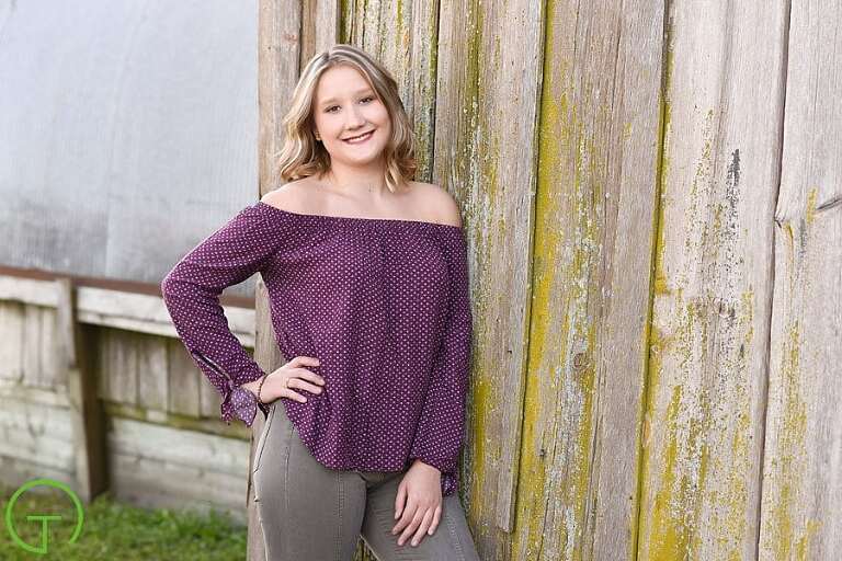 A high school senior poses near a rustic barn for her Ypsilanti senior portrait session.