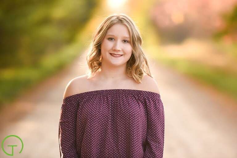 A high school senior poses for her Ypsilanti senior portrait on a lush sunlight dirt road