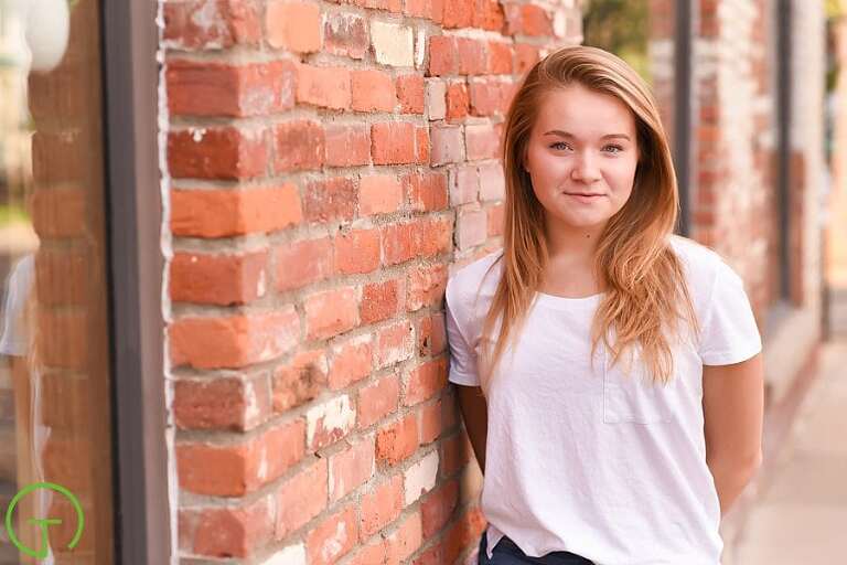 A high school senior poses near an old red brick building in Ann Arbor's Kerrytown during her senior portrait session
