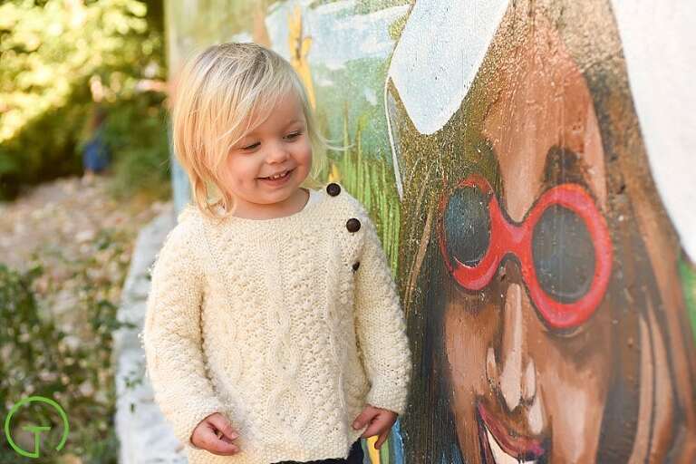 A toddler smiles at a painted face on a mural in Ypsilanti during her Depot Town Portrait Session