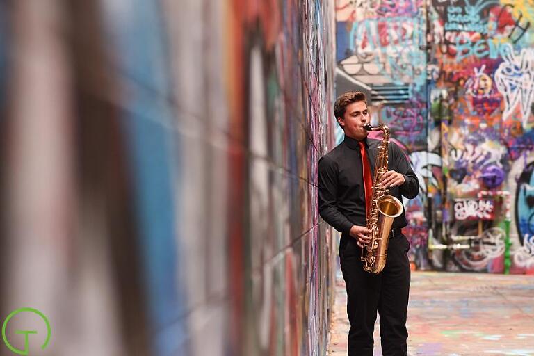 A high school senior playing a saxophone in Ann Arbor's Graffiti Alley for his portrait session