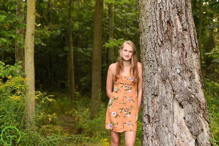 A high school senior poses near an old tree for her ypsilanti senior portrait session