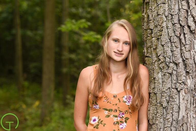 A high school senior poses near an old tree in the woods for her ypsilanti senior portrait session