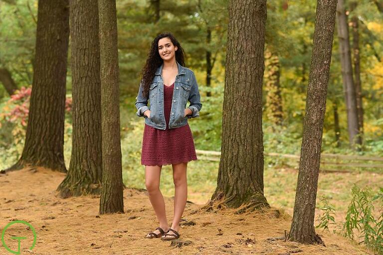 A high school senior poses surrounded by trees for her senior portrait session at Nichol’s Arboretum 