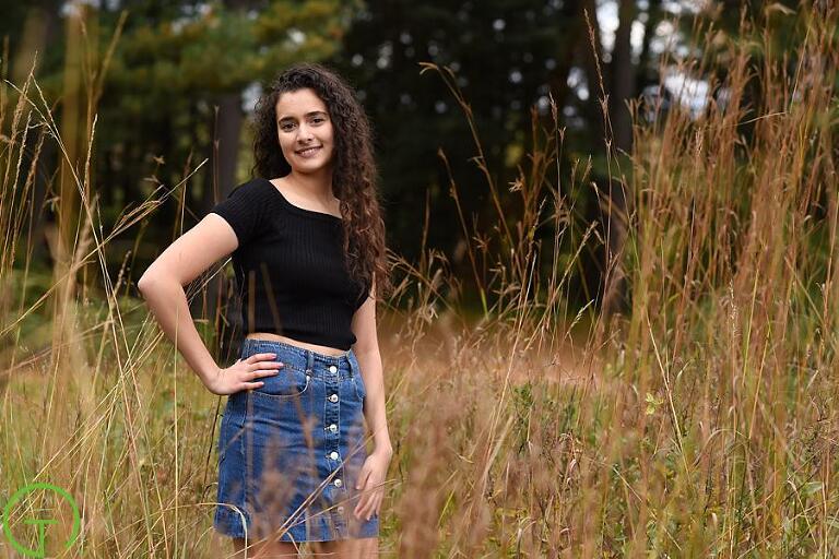 A high school senior poses in a lush grassy field at Nichols Arboretum for her senior portrait session