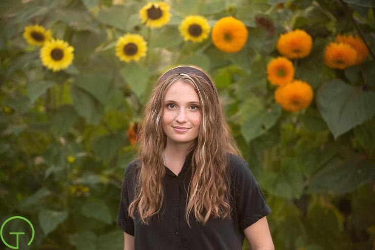 A teenage girl poses with sunflowers behind her for a senior picture