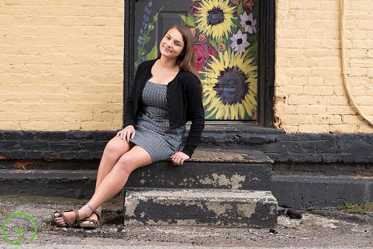 A high school senior sits on a step of a old brick building for her senior picture