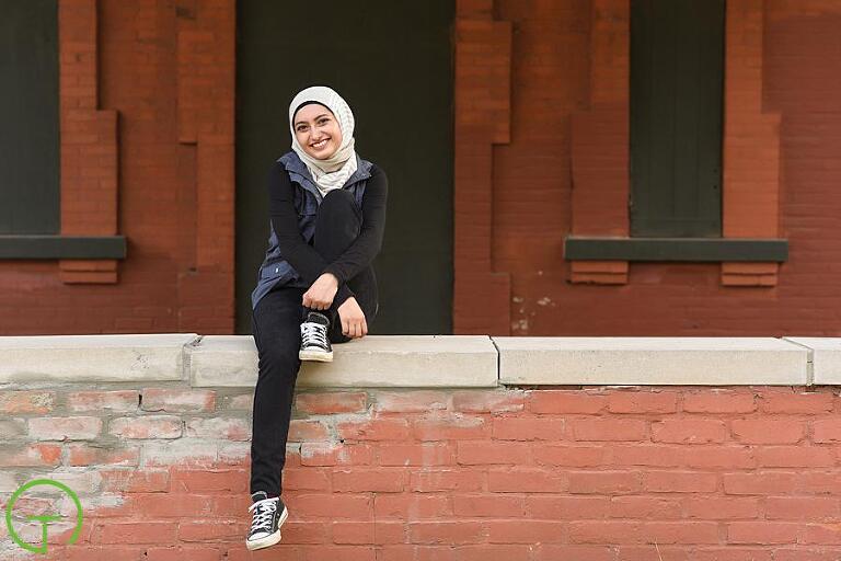 A teenage girl poses on a red brick ledge for her senior pictures