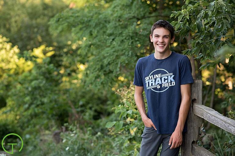 A male high school senior poses at Nichols Arboretum surrounded by green foliage