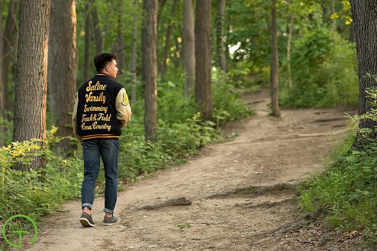 A teenage boy walks on a wooded path for his senior portraits
