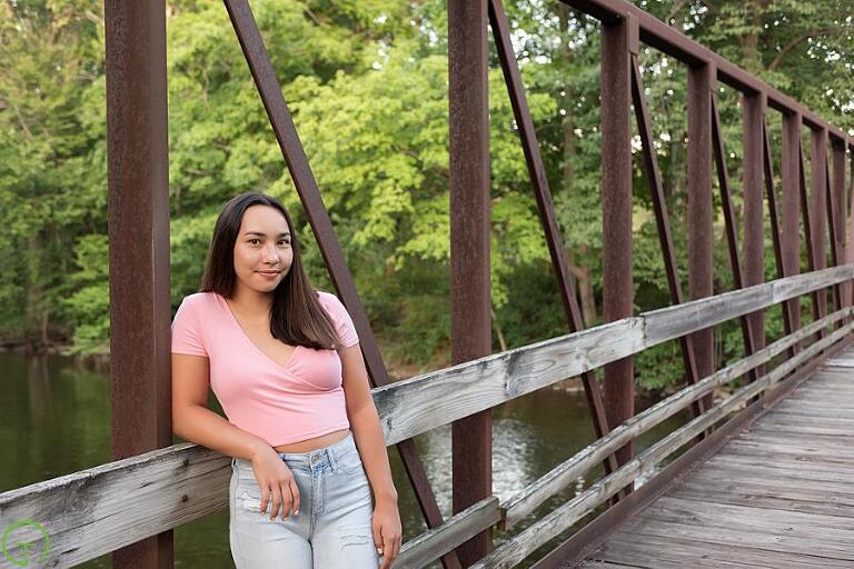 a high school senior poses on a rustic bridge during a senior portrait session