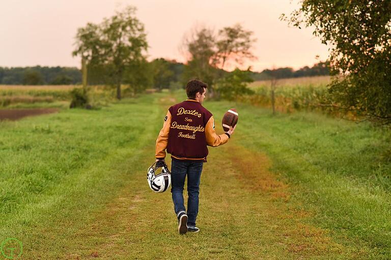a high school football player walks along a lush green path tossing a football 