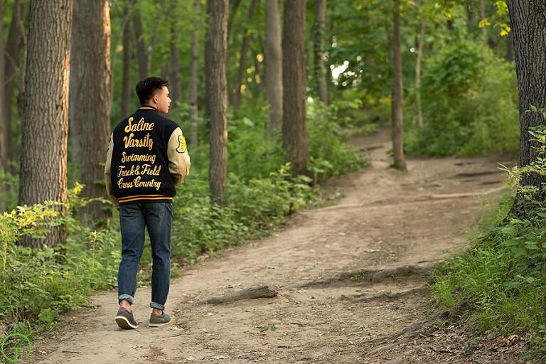 a high school senior boy walks along a wooded path in nichols arboretum
