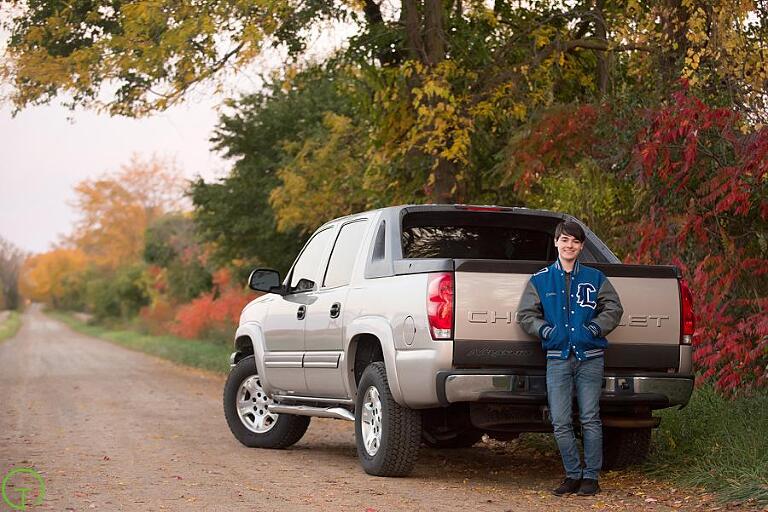 a teenage boy poses near his truck on a courtry road for a senior picture