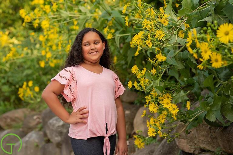 A girl stands near brillian yellow flowers