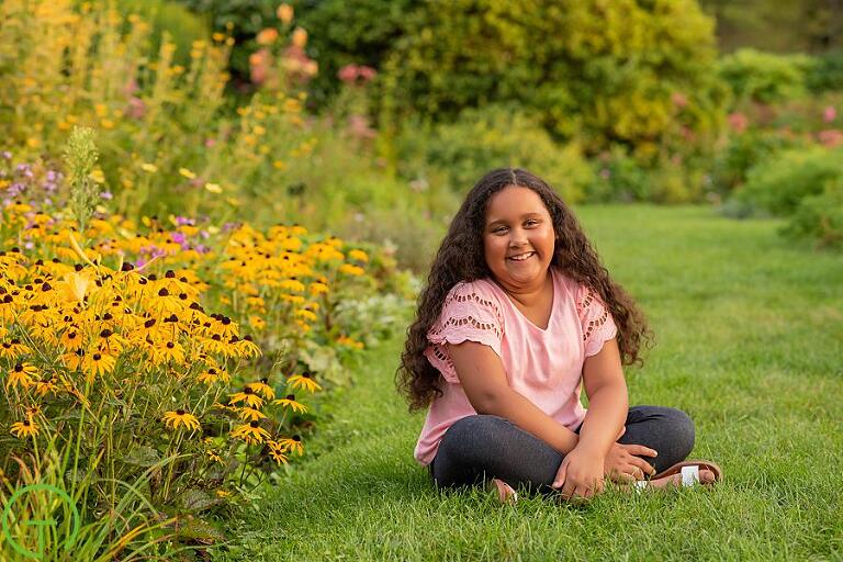 A young girls sits near a bed of bright yellow flowers for her Matthaei Botanical Gardens portrait session